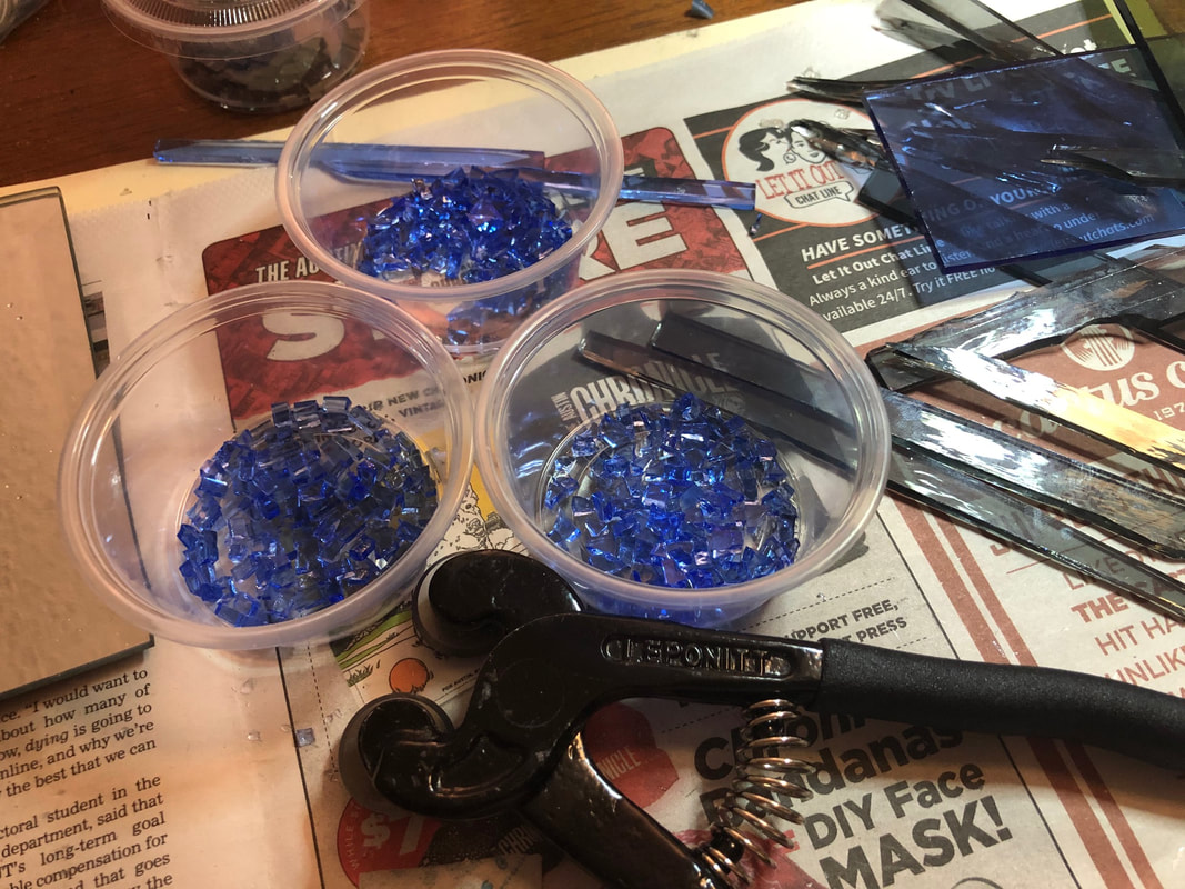 A picture of cut blue glass in little cups next to glass nippers and strips of cut glass.